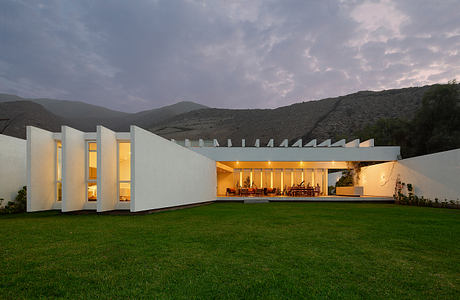 A modern, minimalist house nestled in the mountains, featuring an expansive outdoor patio.