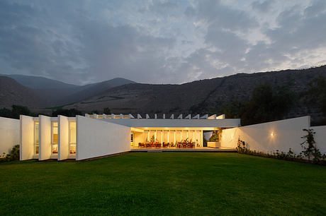 A modern, minimalist building with large windows and a open floor plan set against a hilly landscape.