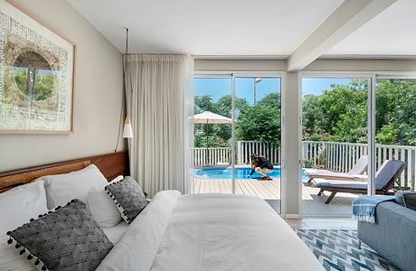 Airy bedroom with sliding glass doors overlooking an outdoor pool and lush greenery.