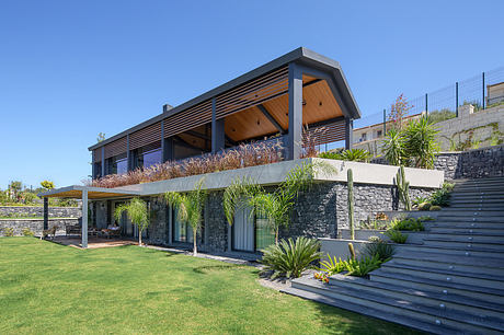 A contemporary house with a wooden and stone facade, surrounded by lush tropical greenery.