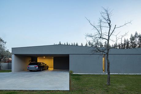 A modern, minimalist garage building with a dark exterior and sleek design. The car inside is visible through the open garage door.