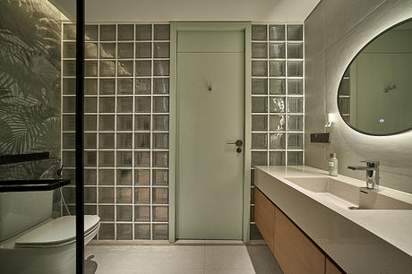 A modern bathroom with a glass block wall, concrete vanity, and round mirror.