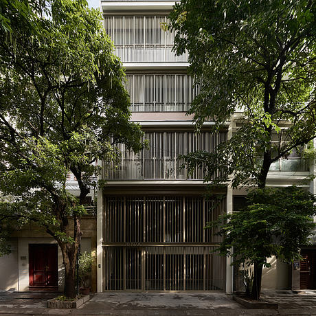 Modernist building with grid-like facade and tall trees surrounding the entrance.