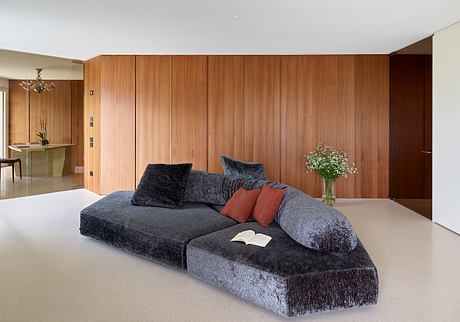 Spacious living room with wood-paneled walls, plush gray sectional sofa, and floral decor.