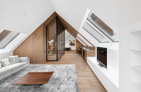 Spacious attic living space with wooden panels, sloped ceilings, and sleek furniture.