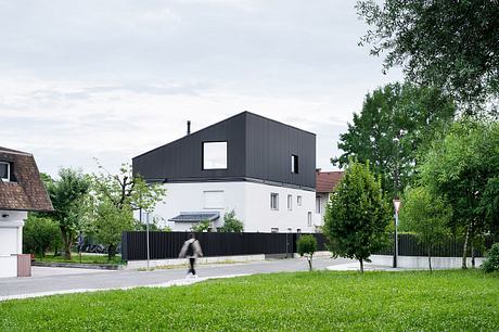 A modern, minimalist house with a black exterior, large windows, and a grassy yard.