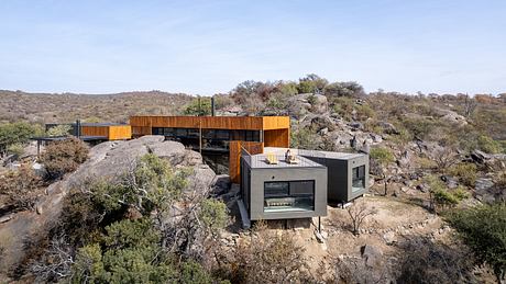 A modern, multi-level house nestled among rocky hills and desert vegetation.