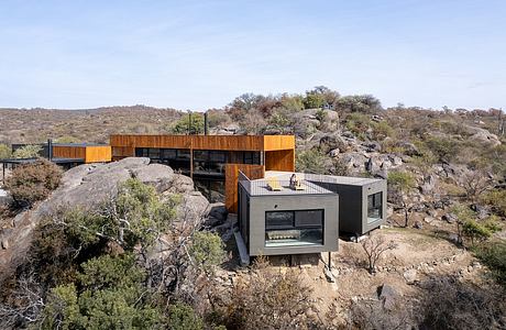 A modern, multi-level house nestled among rocky hills and desert vegetation.