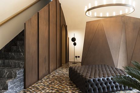 Luxurious interior with dark marble, wooden panels, and a tufted leather sofa under a circular light.