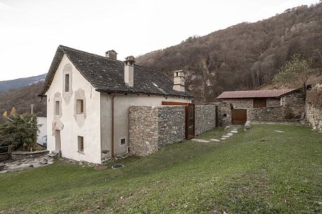 Traditional stone and plaster buildings with tiled roofing nestled in a lush, mountainous landscape.