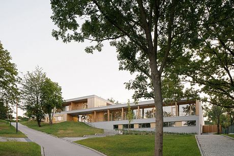 Modern, two-story building with a mix of wood and glass elements, surrounded by lush greenery.