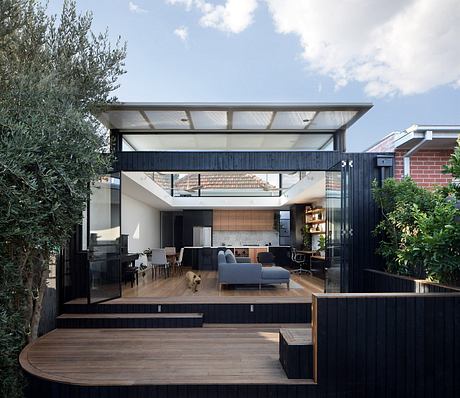 Modern home with sleek black exterior, expansive glass walls, and wood deck blending indoor-outdoor living.