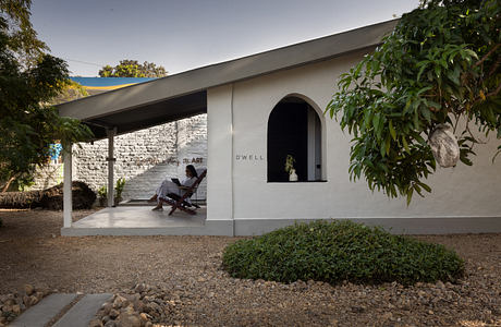 A modern, minimalist building with an arched entryway and a person sitting on the porch.