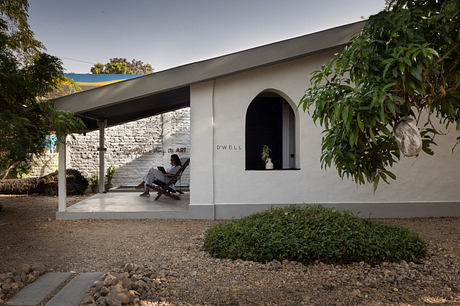 A modern, minimalist building with an arched entryway and a person sitting on the porch.