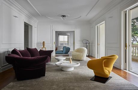 Elegant living room with high ceilings, plush velvet sofa, and modern sculptural chairs.