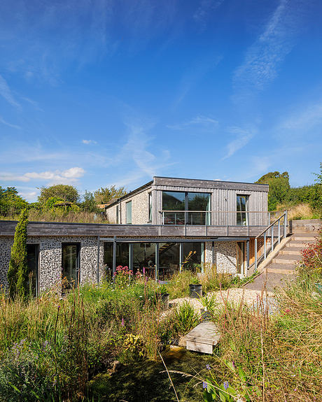 A modern, wooden house with large windows surrounded by lush greenery and a natural landscape.