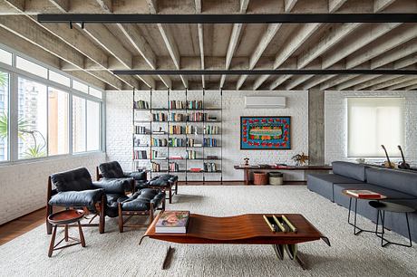 Spacious loft with exposed concrete beams, wall-to-wall bookshelves, and mid-century modern furnishings.