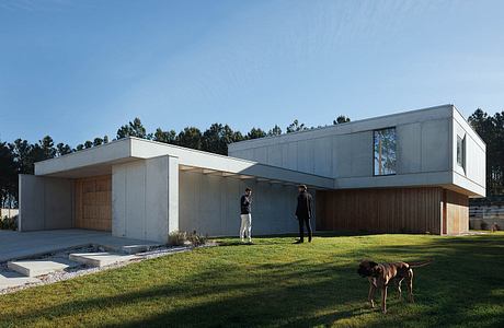 A modern, minimalist residential building with clean lines, large windows, and a grassy lawn.