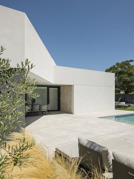 Modern, minimalist house with clean lines, glass doors, and a pool surrounded by lush greenery.