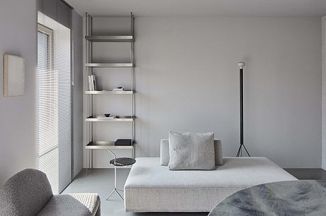 Modern minimalist living room with grey sofa, metal shelving, and floor lamp.