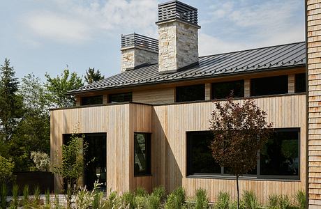 A modern rustic home with stonework chimneys, wooden siding, and large windows.