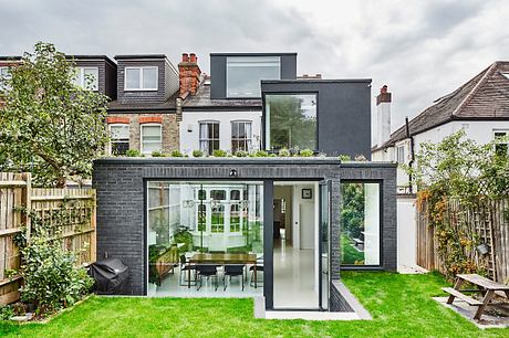 A modern, minimalist home extension with large glass windows, brick exterior, and lush greenery.