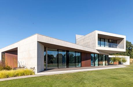 Modern, minimalist structure with glass walls, textured facade, and slanted roofs.