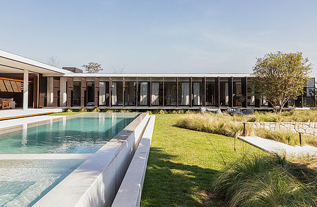 Modern single-story building with large glass panels, surrounded by a pool and lush greenery.