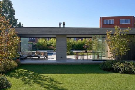 A modern outdoor patio with glass walls, sunken seating area, and lush landscaping.