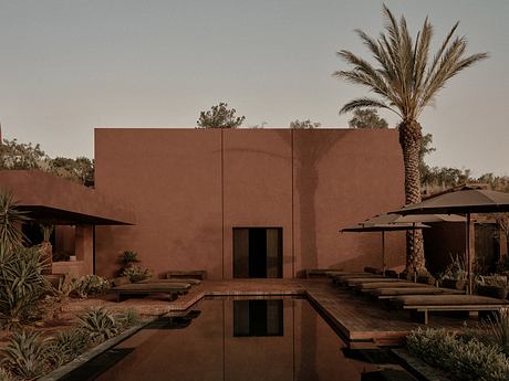 Striking adobe-style building with palm trees, wooden decks, and a reflection pool.