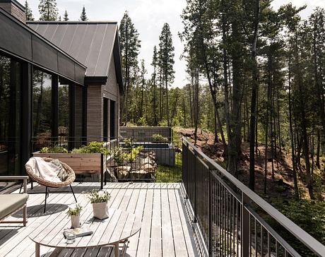 A modern cabin nestled in a lush forest, with an expansive wooden deck and sleek metal roof.