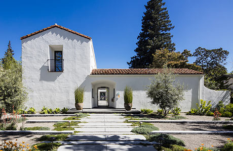 A charming white stucco Spanish-style house with a tiled roof, recessed entry, and ornamental landscaping.