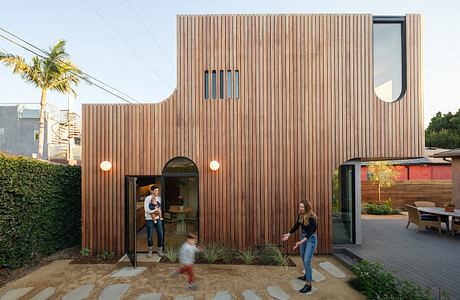 Wooden siding, curved entryway, and outdoor seating area in modern residential design.