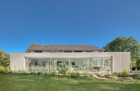 Modern single-story home with large glass windows, surrounded by lush greenery.