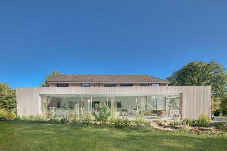 Modern single-story home with large glass windows, surrounded by lush greenery.