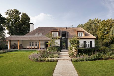 A two-story, thatched-roof house with a stone walkway, landscaped garden, and wooden accents.