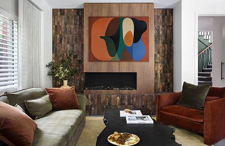 Warm, cozy living room featuring a modern abstract artwork, wood-paneled fireplace, and plush furnishings.