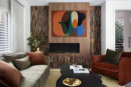 Warm, cozy living room featuring a modern abstract artwork, wood-paneled fireplace, and plush furnishings.