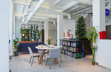 A modern, industrial-style office space with open seating areas, bookshelves, and potted plants.