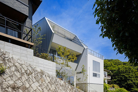 A modern, angular building with glass walls and a stone facade, surrounded by lush greenery.