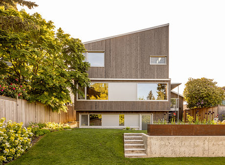 Modern, multi-level home with wood siding, large windows, and landscaped yard.