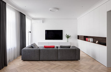 Modern, minimalist living room with gray sectional sofa, flat-screen TV, and built-in shelving.