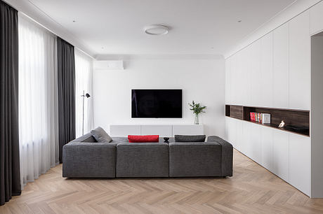 Modern, minimalist living room with gray sectional sofa, flat-screen TV, and built-in shelving.