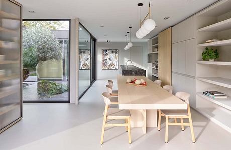 A modern, minimalist dining area with full-length windows overlooking greenery.