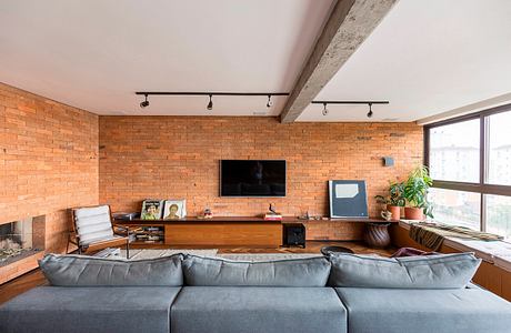 A cozy loft-style living room with exposed brick walls, track lighting, and a large gray couch.