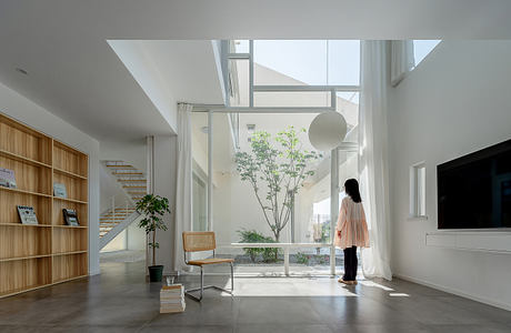 Bright, minimalist interior with large windows, plants, and a wooden bench against the wall.