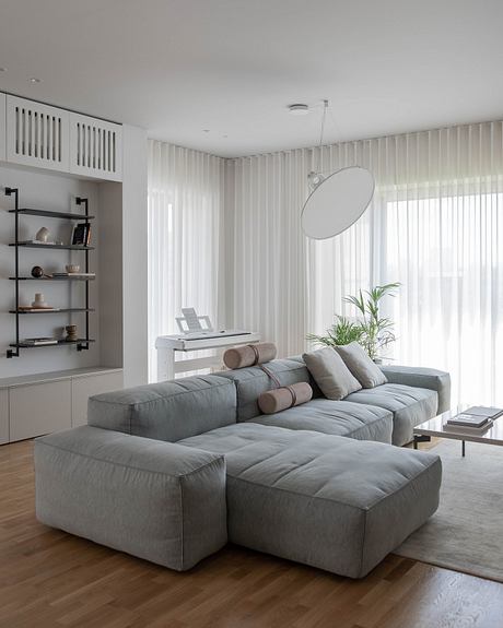 A minimalist living room with a large grey modular sofa, shelving, and pendant lighting.