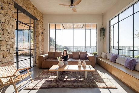 Warm, rustic living space with large windows, stone walls, and cozy seating arrangements.