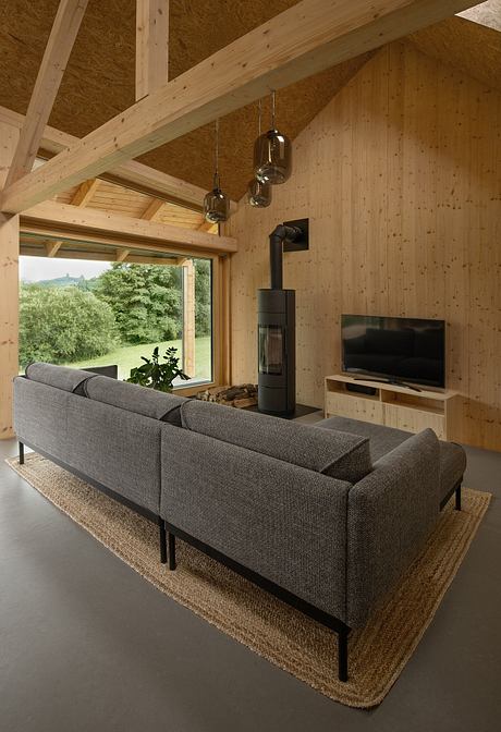 Cozy living room with wooden beams, hanging lights, and a modern, gray couch facing a TV.