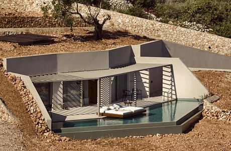 A modern, angular villa with a pool nestled in a rocky, wooded setting.